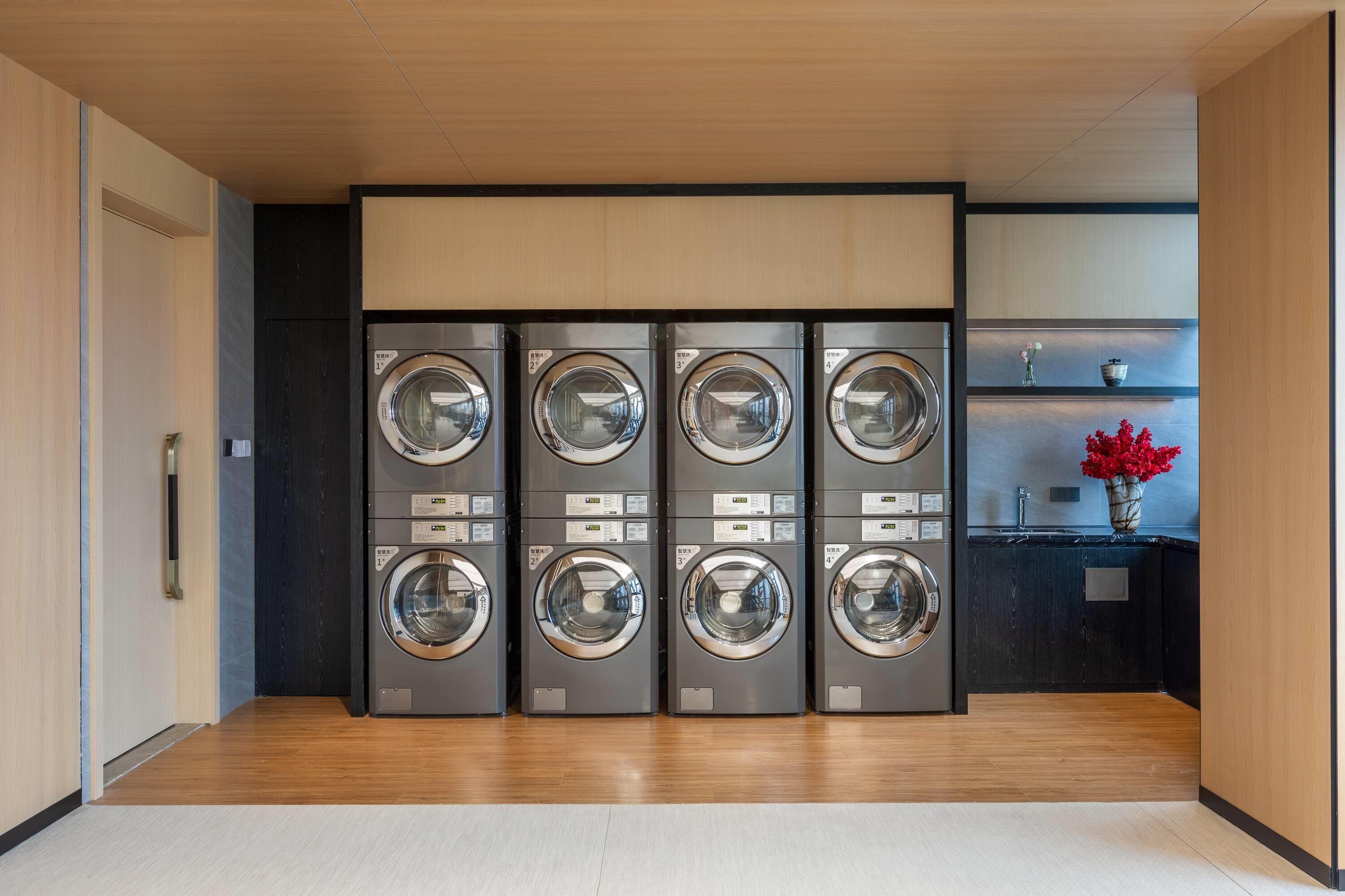 A laundry room with four stacked washing machines, a wooden floor, and a small shelf with flowers.