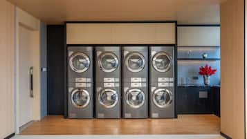 A laundry room with four stacked washing machines, a wooden floor, and a small shelf with flowers.