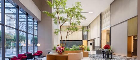A spacious lobby with a central wooden planter, seating area, and large windows offering views of the city.