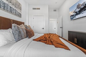 Un dormitorio con cama, almohadas, una colcha, un armario y un cuadro en la pared.