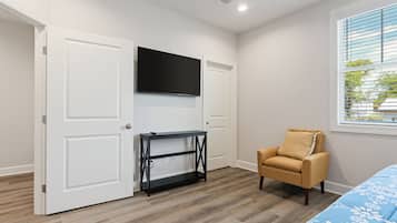 A bedroom with a TV mounted above a black console table, a beige armchair, and a bed with a blue floral bedspread.