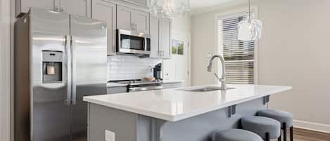 A modern kitchen with a stainless steel refrigerator, a built-in microwave, a water dispenser, and a large island with bar stools.