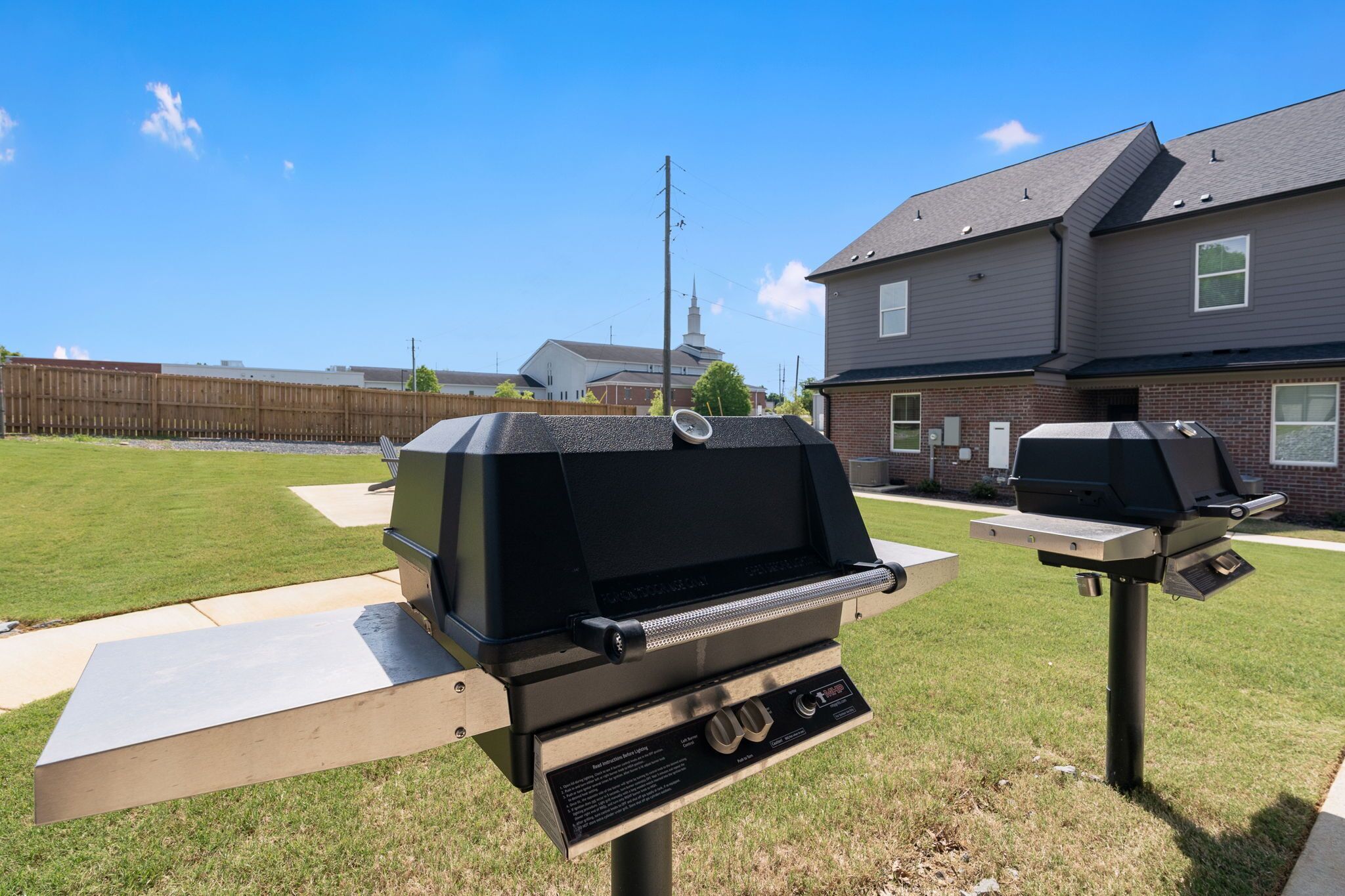 A backyard with two barbecue grills on portable stands, a picnic table, and a wooden fence.