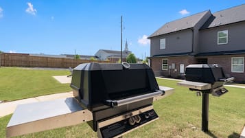 A backyard with two barbecue grills on portable stands, a picnic table, and a wooden fence.
