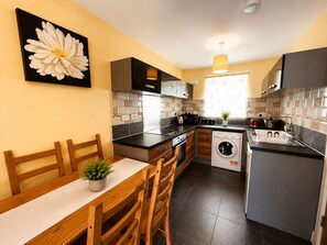 A modern kitchen with a dining area, a washing machine, and a large flower painting on the wall. - Cosy 4 Bed Family Home near Derby City Centre  Rolls Royce (Derby)