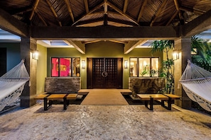 A covered outdoor area with a wooden bench, a hammock, and a stone floor.