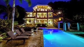 A multi-story hotel with a swimming pool, outdoor seating, and a well-lit entrance. - Vivara: Private House, PH & 5 Villas  180° Ocean View, Dominical CR 8-Guest (Savegre de Aguirre, Puntarenas Province)