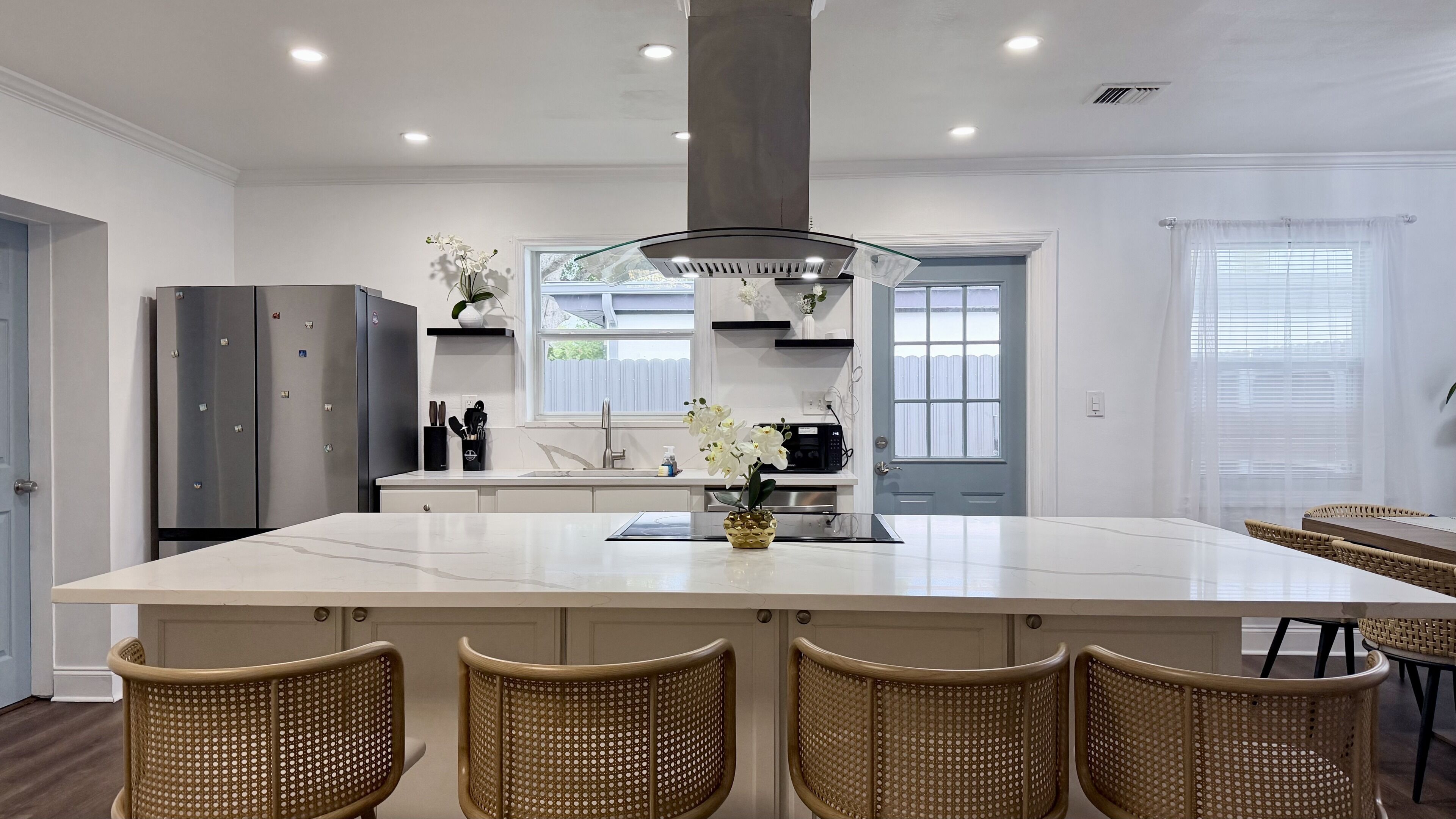 Een moderne keuken met een centraal eiland, inbouwapparatuur en rieten stoelen.