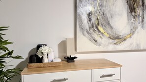 A modern room with a minimalist design, featuring a white dresser with drawers, a black speaker, a woven basket, and a vase with white flowers. - S. Tampa Retreat w/ Chef Kitchen (Tampa)