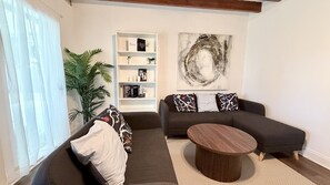 A living room with a dark grey sofa, a round coffee table, and a bookshelf with decorative items. - S. Tampa Retreat w/ Chef Kitchen (Tampa)