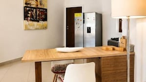 Una cocina con una mesa de madera, dos sillas, un refrigerador y lámparas colgantes.