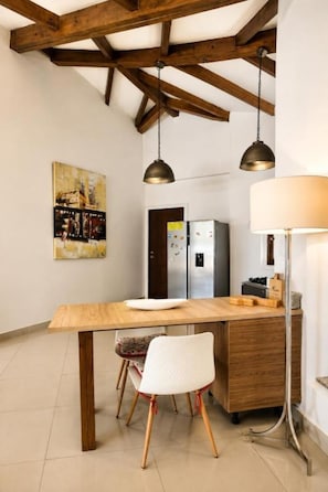 A kitchen with a wooden table, two chairs, a refrigerator, and pendant lights.