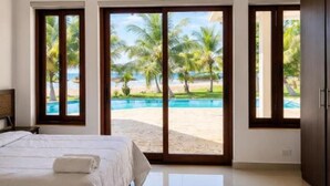 Une chambre d’hôtel avec un grand lit, un deuxième lit plus petit, et une vue sur une piscine et des palmiers.