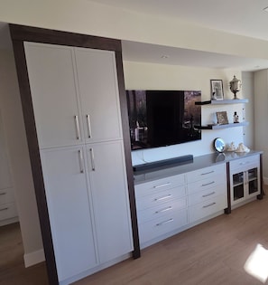 Un salon moderne doté d’un téléviseur à écran plat, de meubles blancs et d’un plancher en bois.