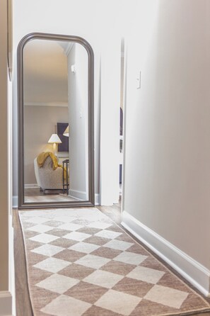 A hallway with a checkered carpet leading to a room with a lamp and a chair.