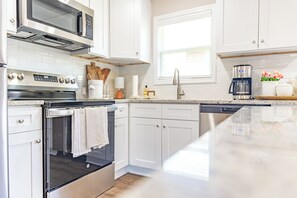 A modern kitchen with white cabinetry, a built-in oven, a microwave, and a coffee maker.