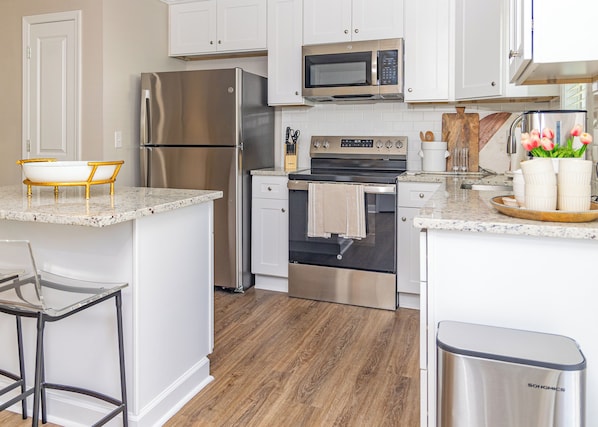 A modern kitchen with stainless steel appliances, a wooden island, and a bar stool.