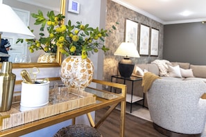 A living room with a sofa, a coffee table with decorative items, a lamp, and a wall-mounted thermostat.