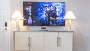 A flat-screen TV mounted on a wall above a glass-top console with two lamps on either side.