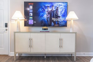 A flat-screen TV mounted on a wall above a glass-top console with two lamps on either side.