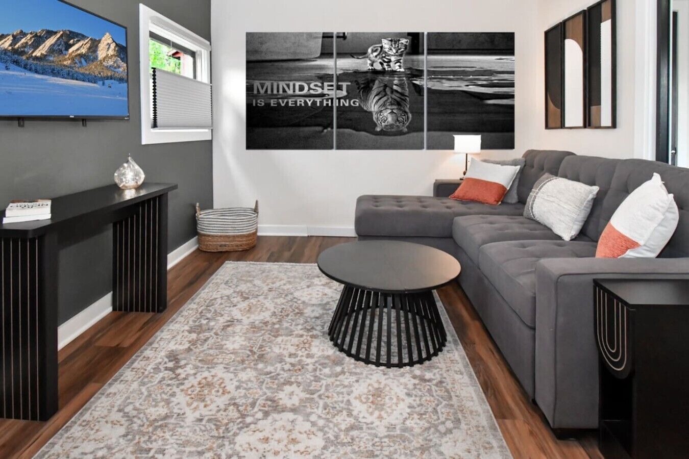Ein modernes Wohnzimmer mit einem grauen Sofa, einem runden Couchtisch und einem großen Wandbild.