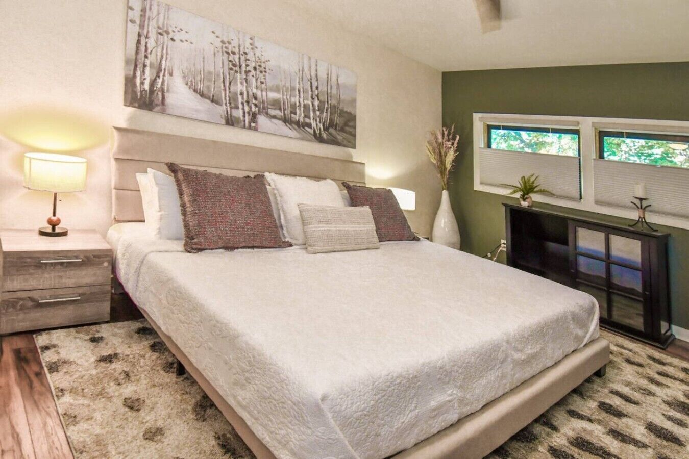 A bedroom with a bed, a nightstand, a lamp, a painting, and a window.