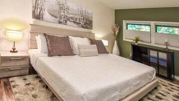 A bedroom with a bed, a nightstand, a lamp, a painting, and a window.