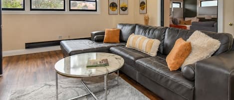 Ein Wohnzimmer mit Ledersofa, einem Glastisch und Blick ins Freie durch große Fenster.