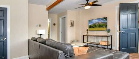 A living room with a sectional sofa, a ceiling fan, and a painting on the wall.