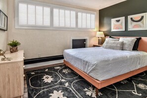 A bedroom with a bed, bedside tables, a lamp, a small cabinet, a potted plant, and a window with blinds. - The Stonehaven at King`s Ridge | Location! (Boulder)