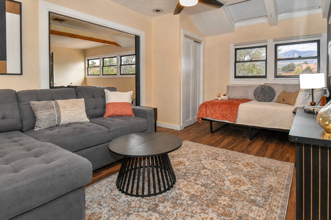 A modern living room with a sectional sofa, a round coffee table, and a bed with a view.