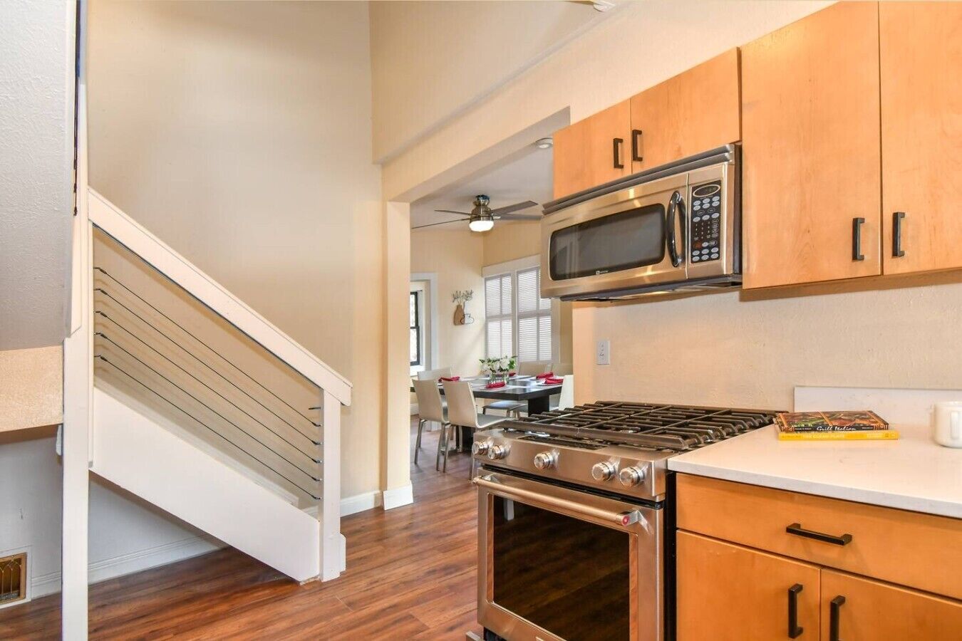 A kitchen with wooden cabinets, a stainless steel stove, a microwave, and a dining area in the background.