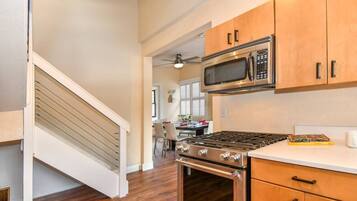 A kitchen with wooden cabinets, a stainless steel stove, a microwave, and a dining area in the background.
