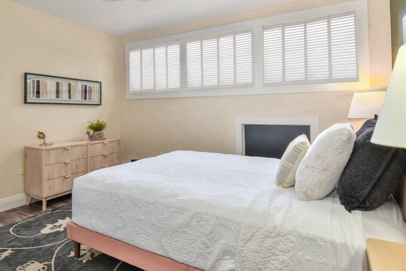 Un dormitorio con cama, cómoda, persianas y un cuadro en la pared.