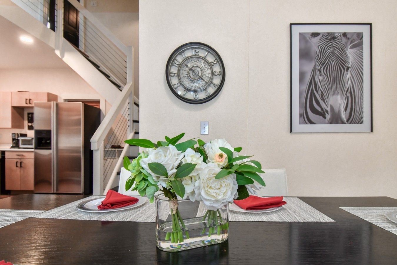 Un comedor con una mesa dispuesta para dos, un reloj de pared y una obra de arte con cebra enmarcada.