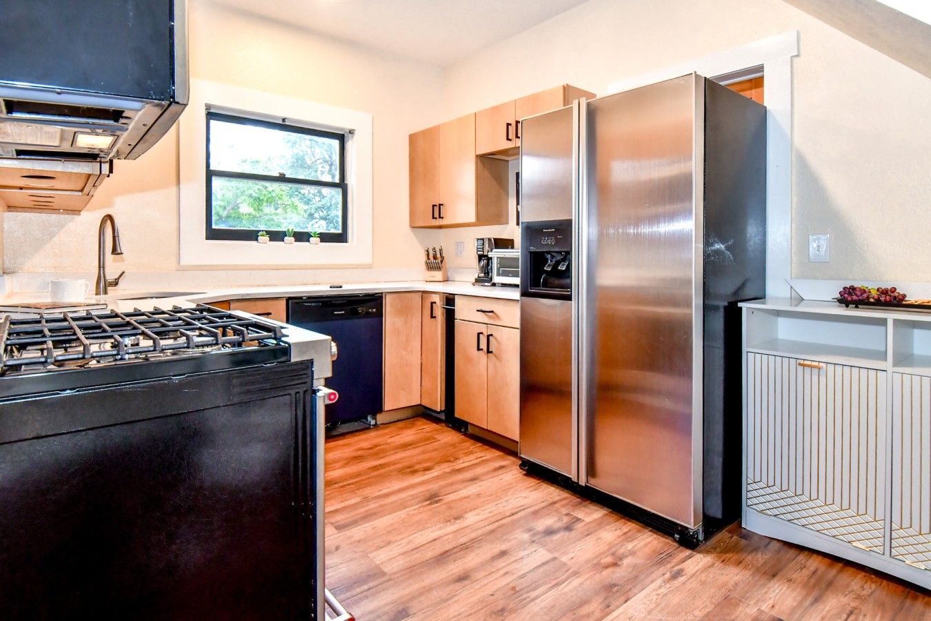 Una cocina moderna con estufa a gas, electrodomésticos de acero inoxidable, armarios de madera y ventana con vistas al verdor.