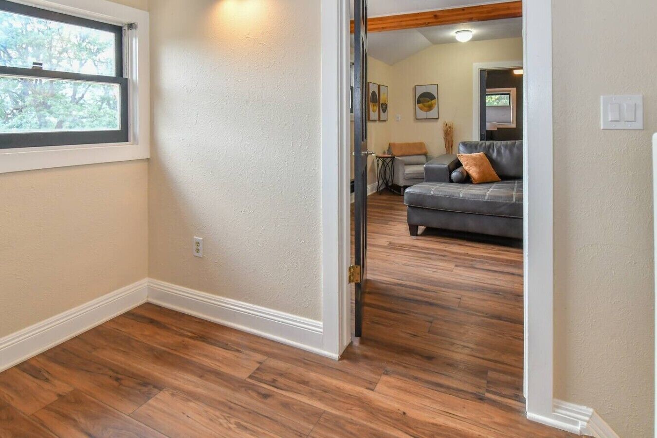 Un pasillo con suelo de madera que conduce a una sala de estar con un sofá gris y un ventanal.