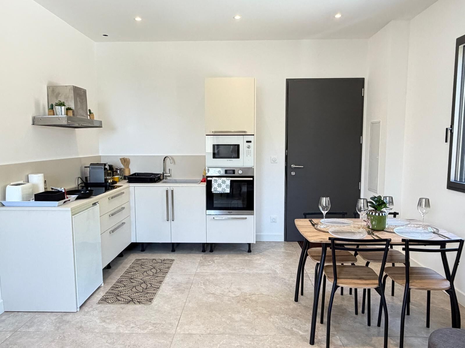 A modern kitchen with white cabinets, a built-in oven, and a dining area with a table and chairs.