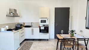 A modern kitchen with white cabinets, a built-in oven, and a dining area with a table and chairs.