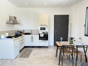 Una cocina moderna con armarios blancos, horno empotrado y un comedor con mesa y sillas.