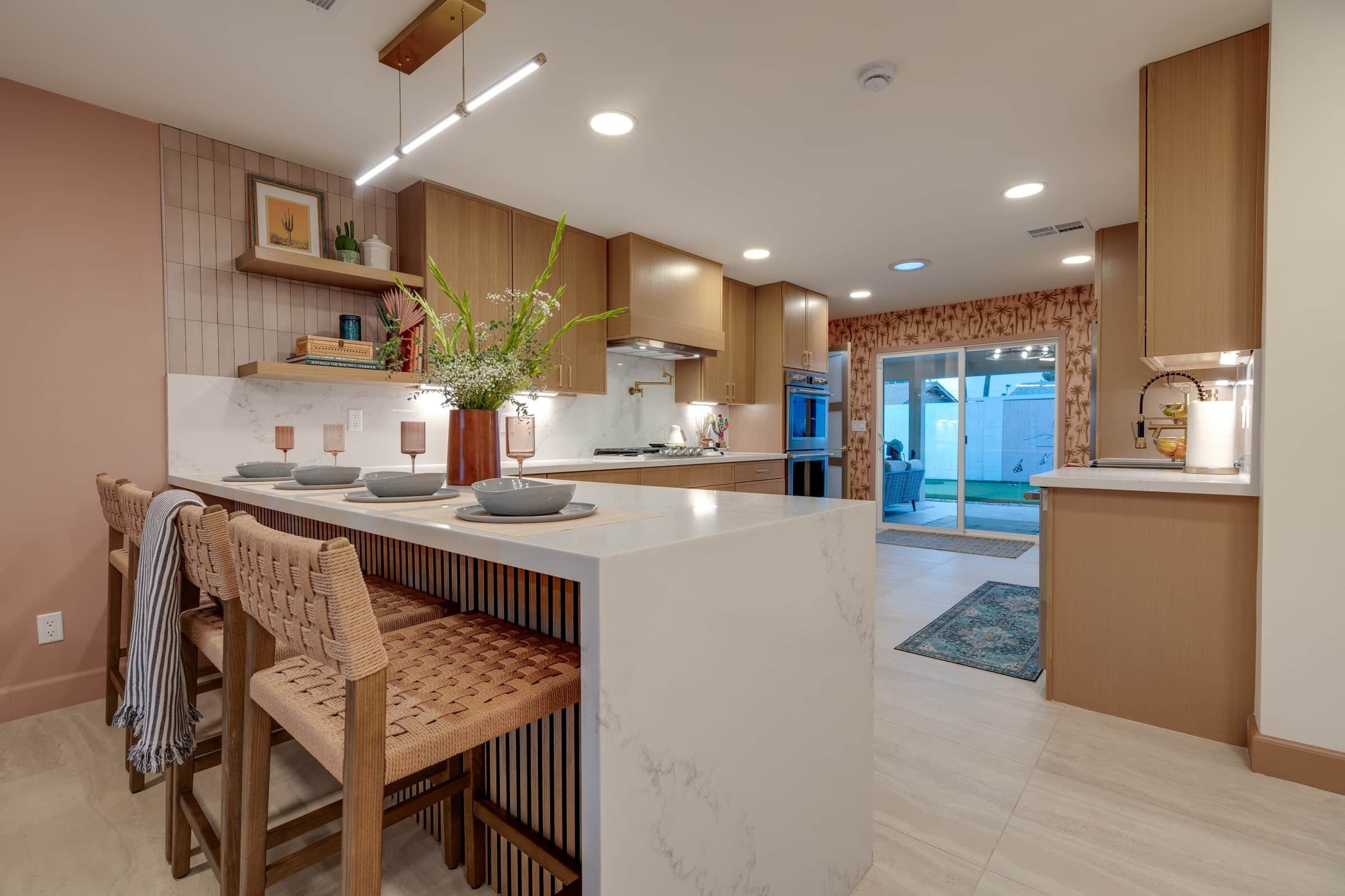 Una cocina moderna con una isla central, muebles de madera y un comedor con sillas de ratán.