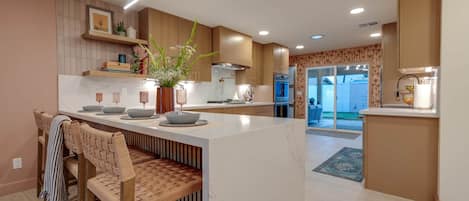 Una cocina moderna con una isla central, muebles de madera y un comedor con sillas de ratán.