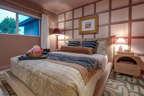 A hotel room with a large bed, a bedside table with a lamp, a window with curtains, and a framed picture on the wall. - Velvet Cactus (Scottsdale)