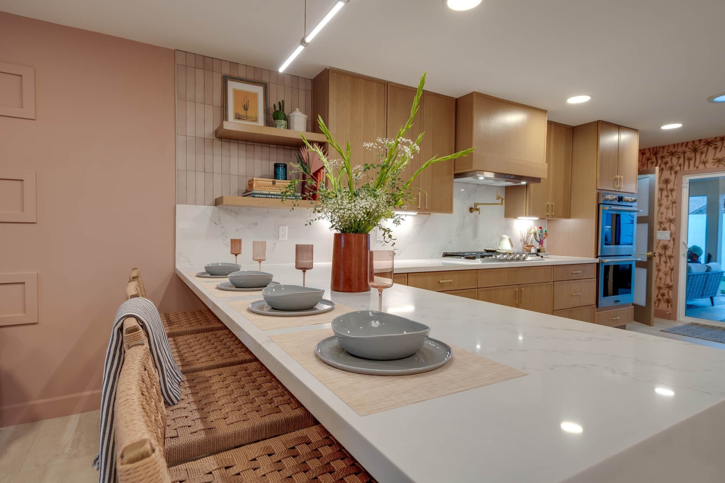 A modern kitchen with a marble countertop, wooden cabinets, and a central island with bowls and a vase of flowers.
