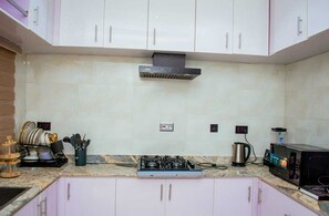 A kitchen with white cabinets, a gas stove, a microwave, and a coffee maker. - The Haven | Modern 3BR En-suite Flat (Ibadan)