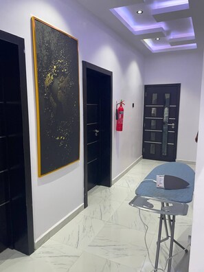 A hallway with a large abstract painting, a fire extinguisher, and a massage table. - The Haven | Modern 3BR En-suite Flat (Ibadan)