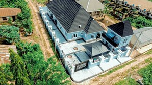 Ein großes, mehrstöckiges Haus mit markantem schwarzem Dach, umgeben von Grünflächen und weiteren Wohngebäuden.