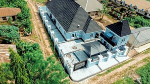 Ein großes, mehrstöckiges Haus mit markantem schwarzem Dach, umgeben von Grünflächen und weiteren Wohngebäuden.