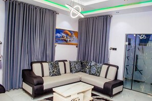 A modern living room with a sectional sofa, a coffee table, and a glass door leading to a balcony. - The Haven | Modern 3BR En-suite Flat (Ibadan)