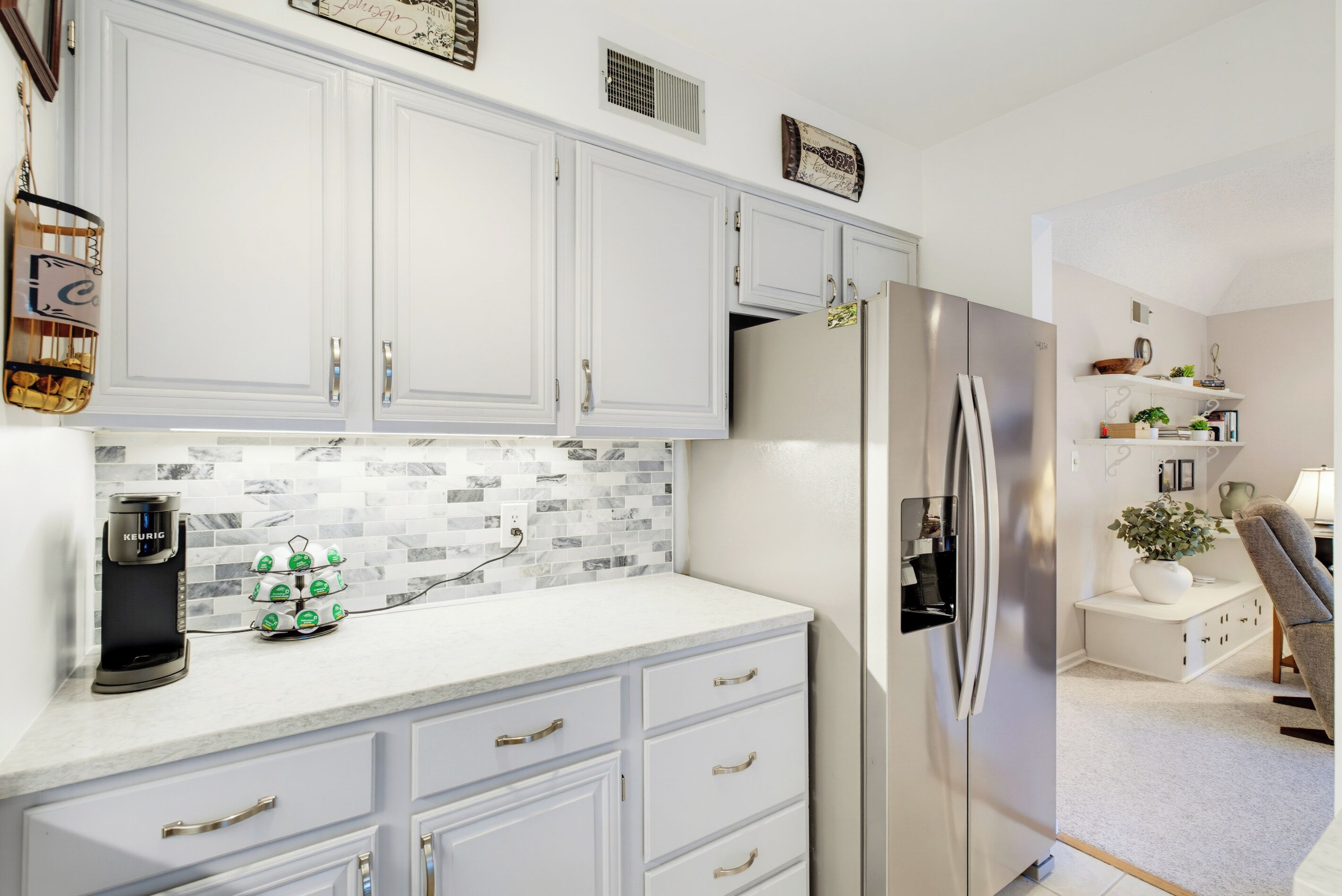 A modern kitchen with white cabinetry, a stainless steel refrigerator, and a coffee machine.